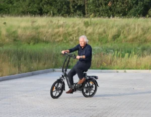 Senior die op een Opmaet Touring vouwfiets rijdt op een parkeerplaats.